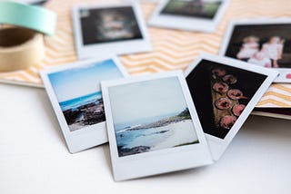 A selection of polaroid photographs sit on a table. The images include beach scenes and people.