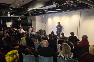 comedian in front of a full crowd in the art space of New Haven