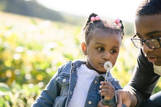 Young girl and man in a field with a dandelion