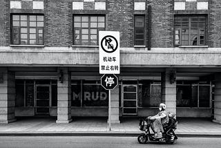 Two people riding a scooter down a quiet street.