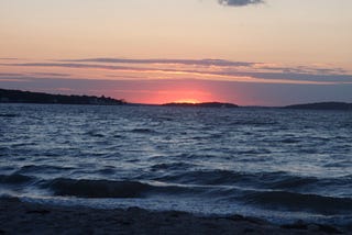 A vanishing pink-purple sunset over choppy bay water