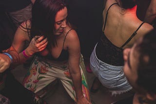 Two young girls dancing close together. They are wearing tank tops and look sweaty.