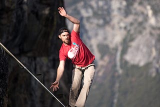 man walking a suspended line between two mountain peaks