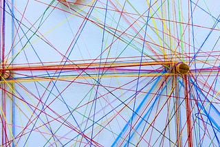 Coloured threads wound around spokes to form a network. Photo by Omar Flores on Unsplash