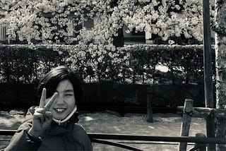Pre-teen Japanese girl giving the peace sign in front of cherry blossoms.