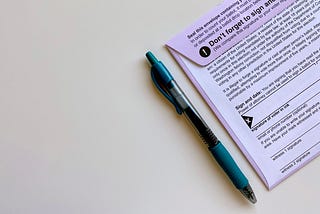 An image of a mail-in ballot lying on a table next to a blue pen.