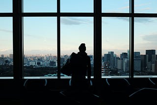 Silhouette of a woman in a high rise office staring out over a city skyline.