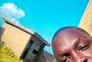 A picture of me sitting at home, the background is made up of the blue sky, green grass and a construction shed. Circa 2020. It reminds me of Mr Eazi’s “One day you will understand” cover art.