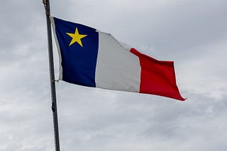 Image of the Acadian flag. It is the French flag with the addition of a gold star in the upper left-hand corner of the flag.