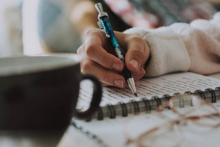 Foto de uma mão feminina escrevendo em um caderno.