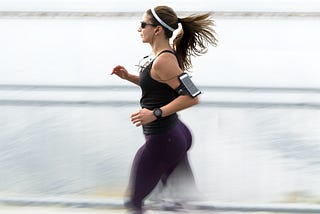 A female runner dressed in black with blurred feet giving the impression of running faster than she is