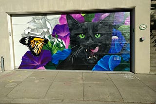 A mural on a garage of a black cat licking its lips as a monarch butterfly floats by.