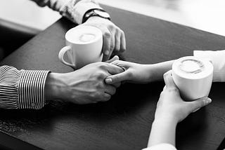 A woman’s hand holding a man’s hand over a cafe table, as the two have coffee. Depositphotos | kotin