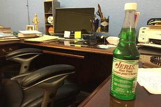 Desk, chair and bottle of Jeris Hair Tonic on top of desk.