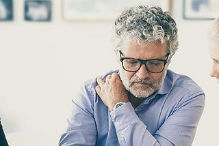 Middle aged father sitting at a table with his two twenty-something daughters. The father is listening to his daughters.