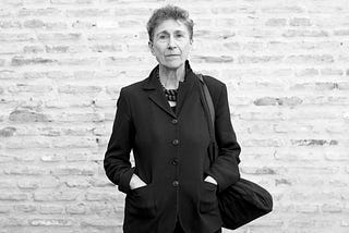 Blanco y negro. Mirando a cámara, Silvia Federici en un saco negro, con su clásico pelo corto. Detrás una pared de ladrillos