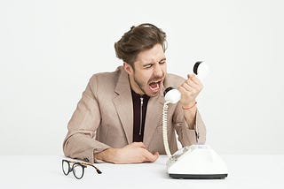 a man in a business suit yelling into an old style telephone