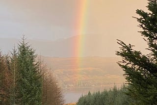 Photo:start or end of a rainbow over a lake, view from woodland path with trees either side.