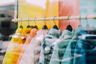 A window display of a rack of brightly colored down jackets