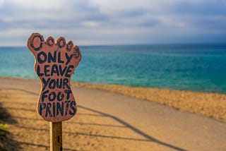 A notice board in the shape of a foot, by the sea, which reads ‘Only leave your foot prints’