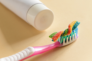 A white tube of toothpaste; a pink toothbrush with a rainbow candy on top