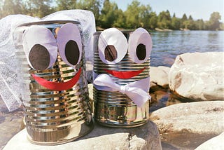 Two cans with cartoon faces are dressed up as a bride and groom.