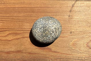 A perfect round grey pebble with a patterned surface, placed on a wooden table.