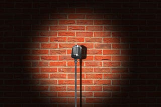 A microphone stand on a stage in a spotlight against a brick wall.