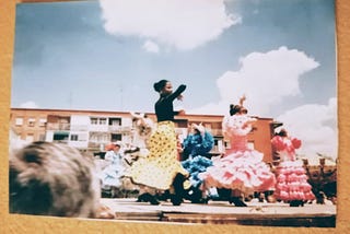 Black child dancing flamenco surrounded by white children. Traditional flamenco dresses.