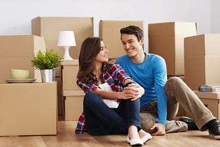 A man and a woman sitting on the floor surrounded by boxes