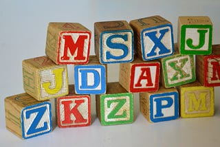 Three stacked rows of worn, colourful wooden blocks with single capital letters of the alphabet carved onto the front of each