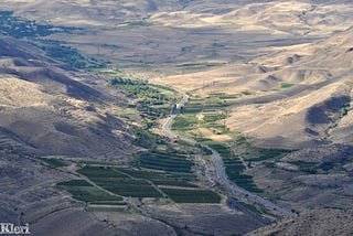 A road in a green valley surrounded by arid mountains.