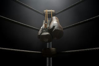 A pair of leather boxing gloves hang off a turnbuckle of a boxing ring