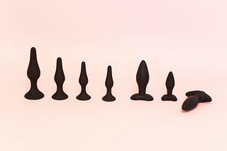 A collection of black bug plugs stand out against a pale pink background.