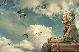 Older woman sits on a bench with a suitcase watching birds flying and clouds floating by,