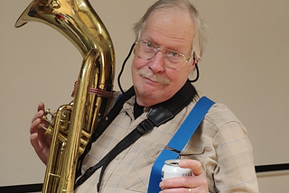 Image of the author with his baritone horn in one hand, a beer in the other, and one of his suspender straps hooked under the thumb of the beer hand.