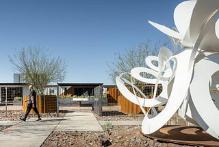 A modern steel sculpture in front of Sparkbox shipping container structures