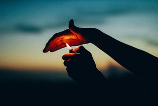 Hands holding a lighter against a twilight sky, creating a little lantern by reflecting the light against the palms.