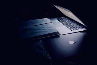 In the dark, a laptop screen illuminates a book