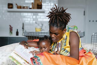 A Black woman reads a book to her child.