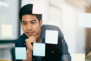 Man considering glass whiteboard covered in Post-It notes