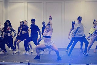 A dancer on stage with backup dancers behind her performing a hiphop dance routine
