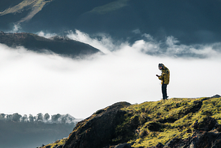 DALL-E generated image based on prompt: “hiker in foreground with a scenic view of mountains in the background with a thick mist enveloping a tree line below, all taken on a high resolution camera”