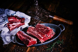 Uncooked high-quality steak fillets on a metal platter, being prepared with salt