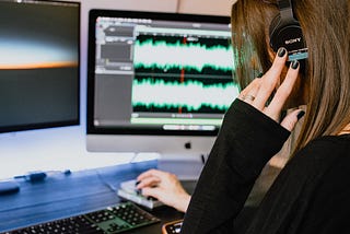 Woman listening to sound played back on sound editing software. She is in a black shirt and has black nail polish and has her hands on the keyboard.