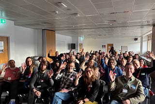 Nearly 60 people at Product for the People #6 waving at the camera, smiling.