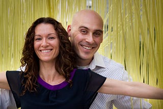 A woman and man smile in front of yellow streamers