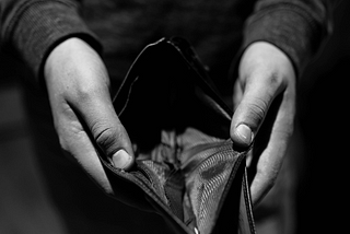 A monochromatic image of a person’s hands holding an empty wallet.