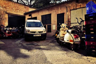 photo of a garage area, a backyard somewhere. Cars and vespas