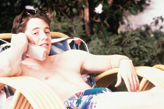 A young man is by the pool on a lounge chair talking on a phone. Ferris Bueller’s Day Off